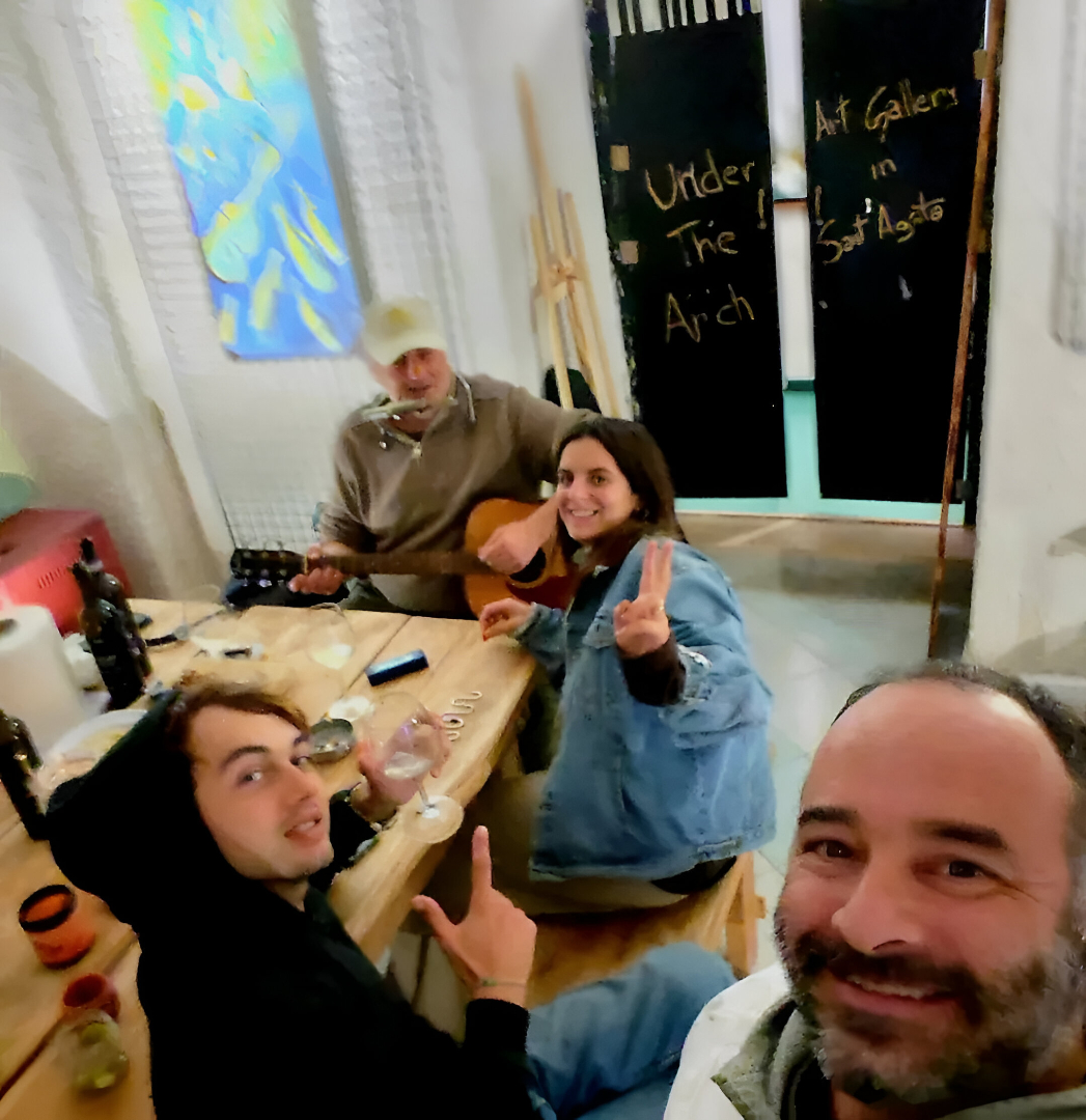 A group of people enjoying a social gathering at Under the Arch Art Gallery, with live guitar music, wine, and a friendly atmosphere.