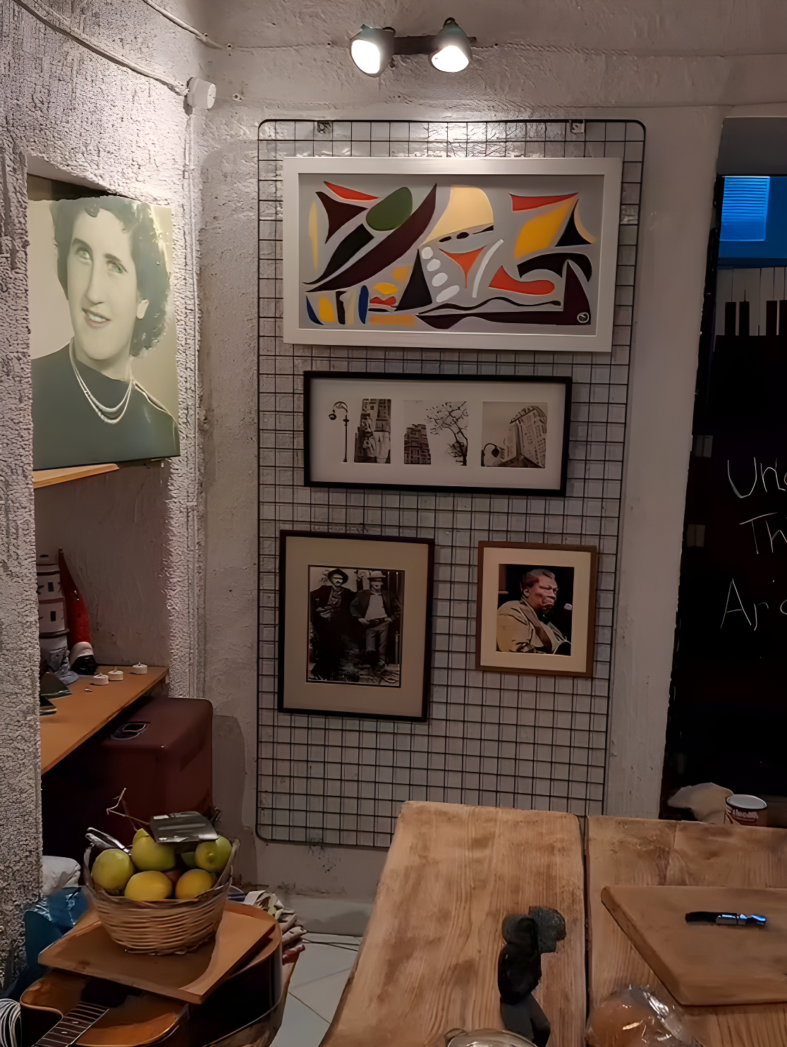 Interior of Under the Arch Art Gallery in Sant’Agata Sui Due Golfi, featuring an exhibition wall with modern paintings, a rustic wooden table, and a basket of local lemons.