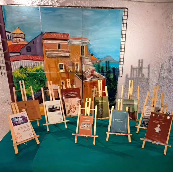 A collection of historical books about the Sorrento Peninsula displayed on small wooden easels in front of a large painting of a local cathedral.
