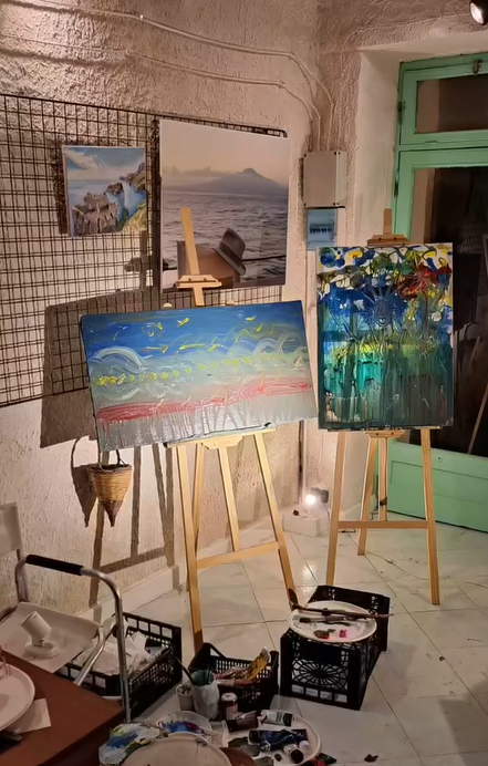 Interior of the art studio at Under the Arch Gallery, featuring several easels with colorful abstract and landscape paintings under warm lighting.